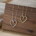 Silver-tone and gold-tone open heart necklaces displayed side by side against a wood block