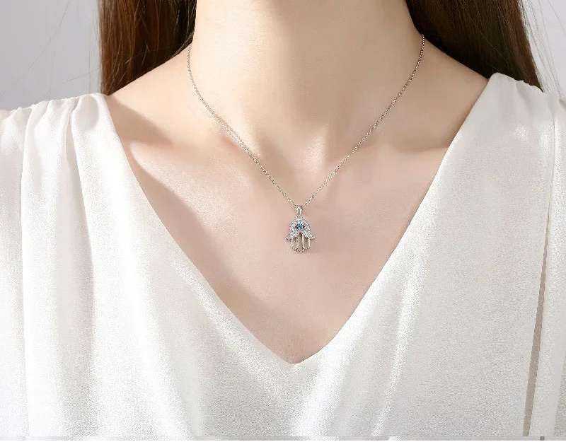 Silver-Tone hamsa hand necklace worn at the neckline with a blue evil eye center