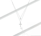 Sterling silver heart and cubic zirconia cross necklace arranged on a white reflective surface