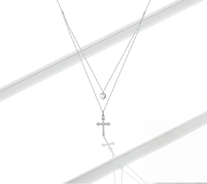 Sterling silver heart and cubic zirconia cross necklace arranged on a white reflective surface