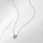 Silver heart necklace displayed on a white curved surface, showing the fine cable chain and stone-set pendant