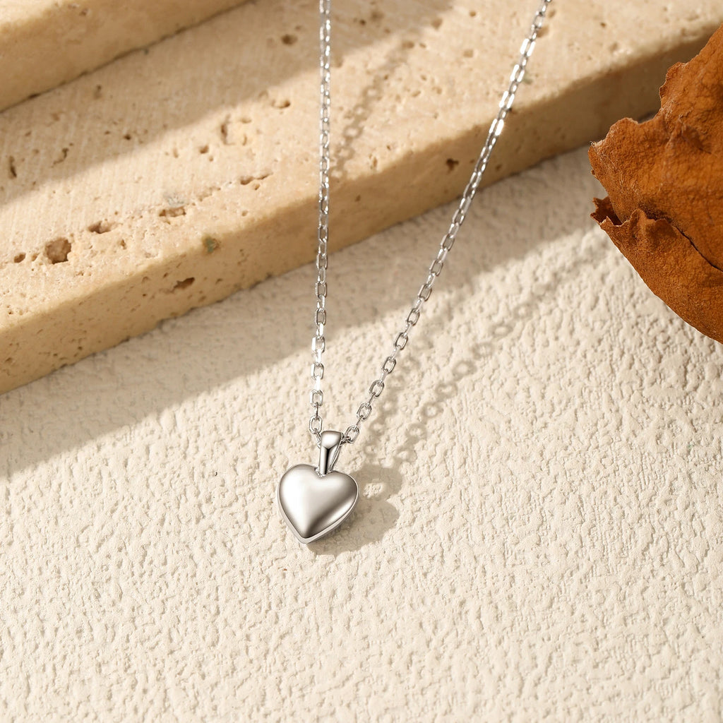 Silver puffy heart pendant displayed on a textured surface with its fine elongated-link chain