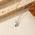 Silver puffy heart pendant displayed on a textured surface with its fine elongated-link chain