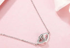 Silver-tone interlocking heart pendant with a clear CZ stone row on a pink surface