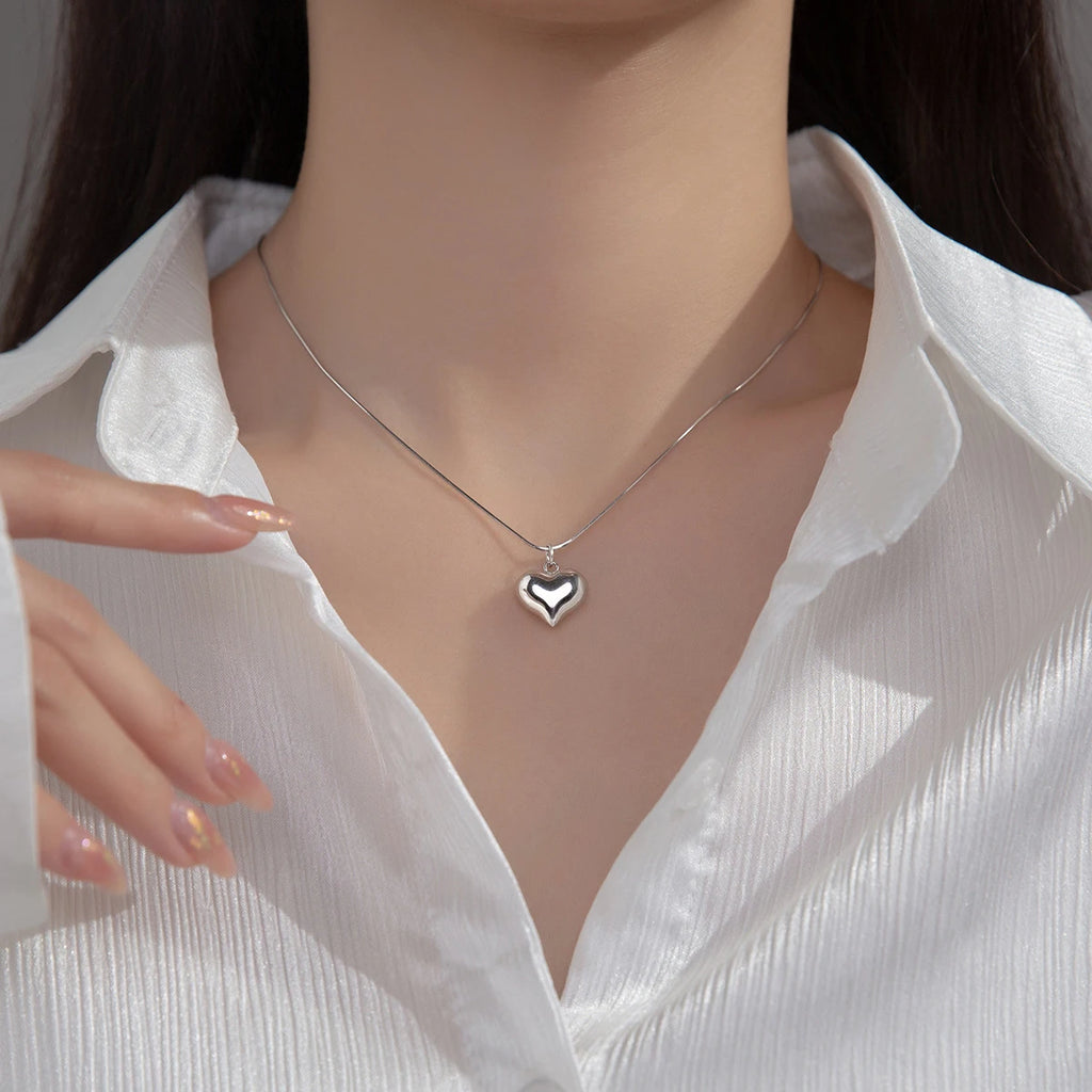 Silver-tone polished heart necklace worn with an open white collar