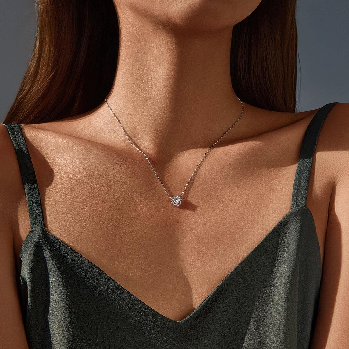 Silver heart pendant necklace worn at the base of the neck with a clear stone-set border