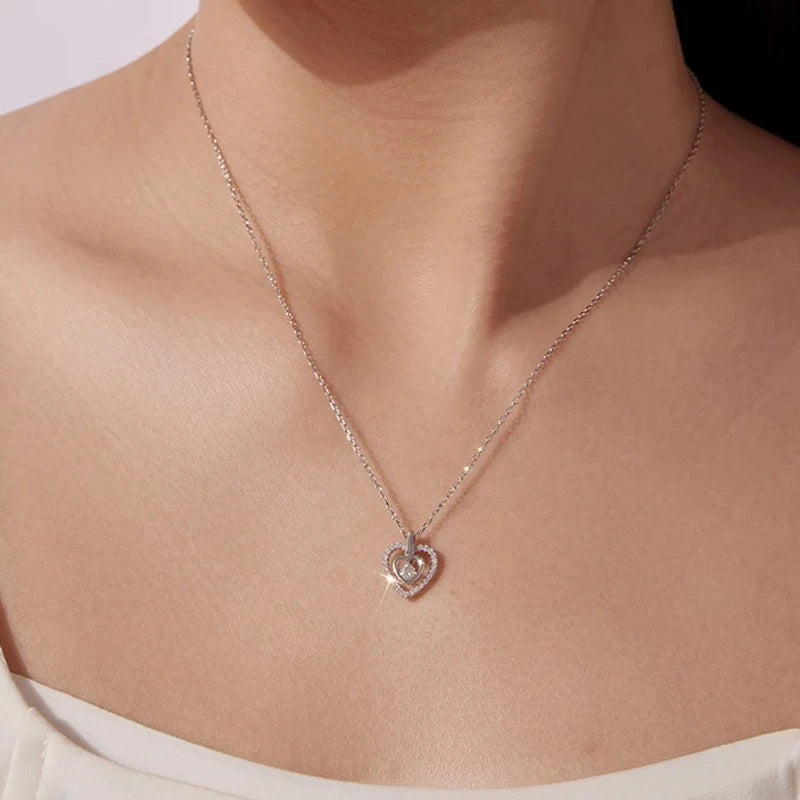 Silver nested heart pendant necklace worn at the collarbone, showing the stone-lined outer heart and center moissanite