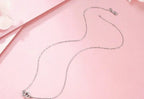 Silver-tone linked heart necklace laid out with an oval-link chain and clasp on pink