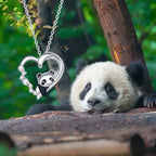 Silver-tone panda heart necklace hanging beside a resting panda in a leafy outdoor scene