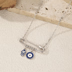 Angled flat lay of the silver safety pin necklace with blue enamel Hamsa and eye charms