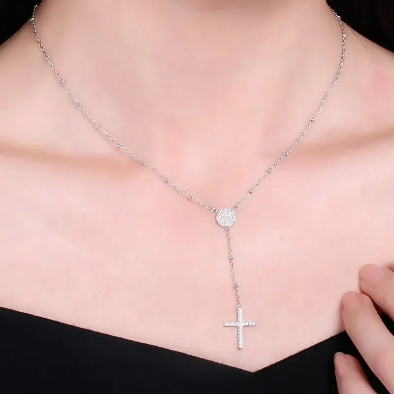 Silver-tone rosary-style necklace worn on the neck, featuring a sparkling round center and cross drop