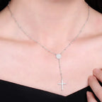 Silver-tone rosary-style necklace worn on the neck, featuring a sparkling round center and cross drop