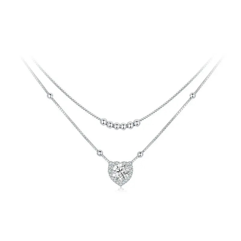 Silver-tone layered heart necklace with polished bead strands and a clear stone-bordered heart on white
