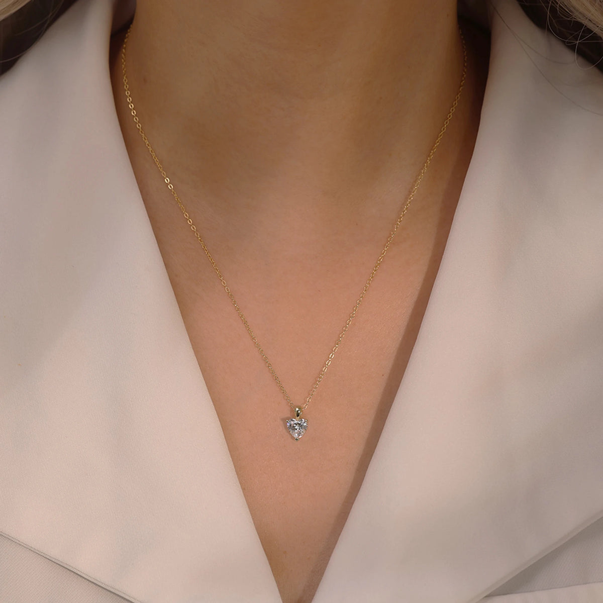 Small gold-tone clear heart necklace worn below the collarbone with a white blazer