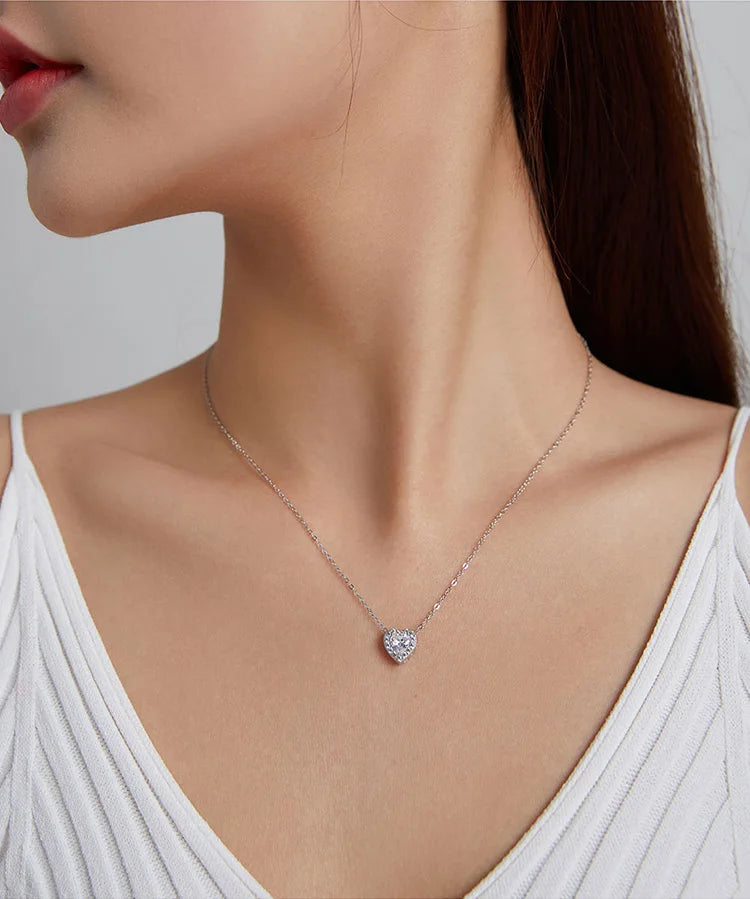 Small clear CZ heart pendant worn on a fine silver-colored chain above a white neckline
