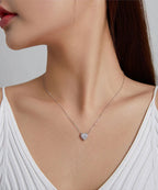 Small clear CZ heart pendant worn on a fine silver-colored chain above a white neckline
