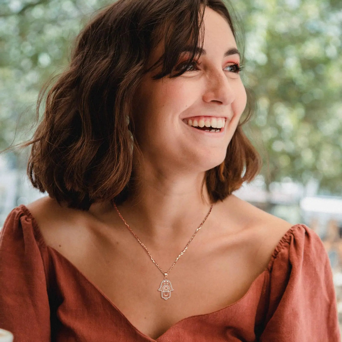Rose gold Star of David Hamsa necklace worn with an off-shoulder top in an outdoor setting