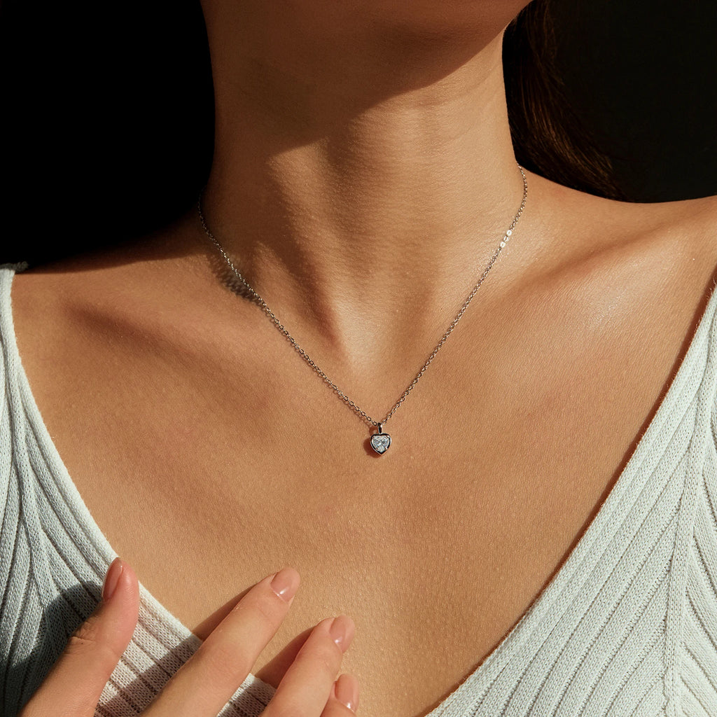 Sterling silver heart necklace worn at the base of the neck with a clear faceted center stone