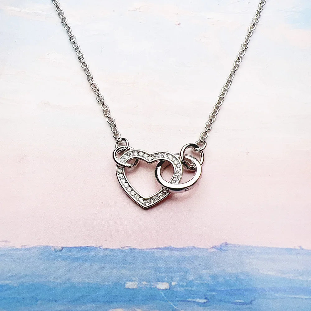 Close-up of the silver-colored necklace with a stone-edged heart and overlapping circular link