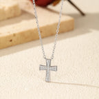 Silver-tone cross pendant with eight moissanite stones displayed on a light textured surface