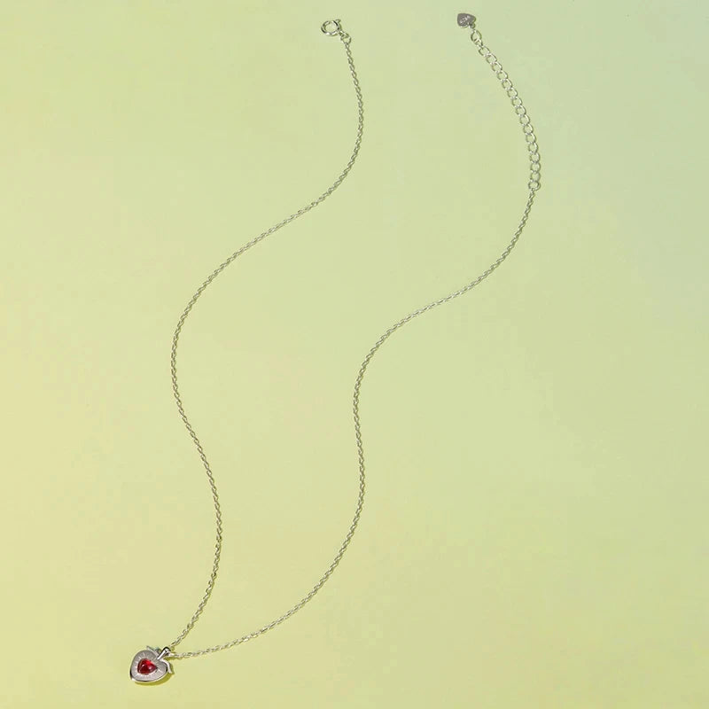 Full strawberry heart necklace laid on a pale yellow background with an adjustable extender