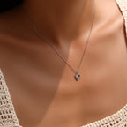 Small sterling silver heart pendant necklace worn at the base of the neck with sunburst rays visible