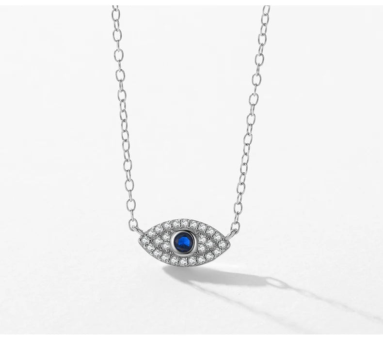 Silver-tone evil eye necklace suspended over white with a clear crystal outline and blue pupil