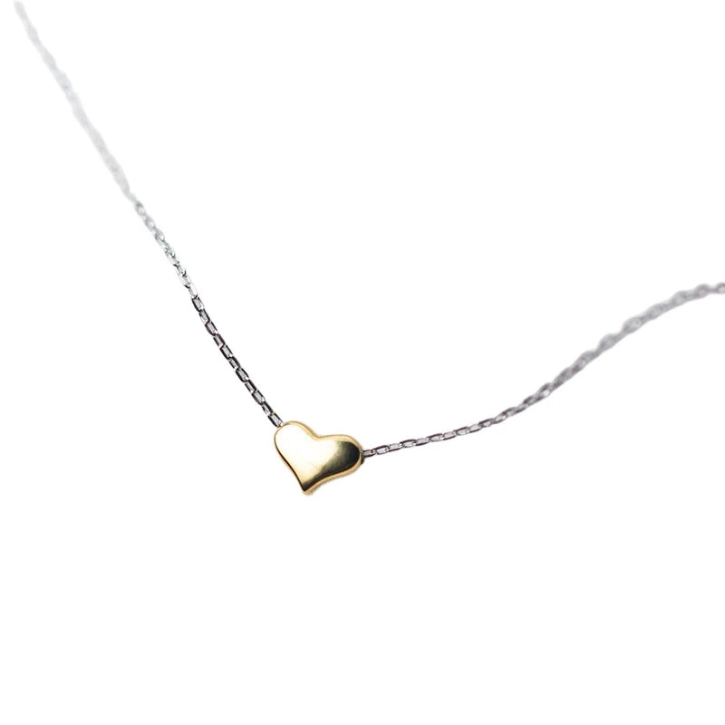 Tiny gold heart necklace with silver-tone link chain arranged on softly draped white fabric