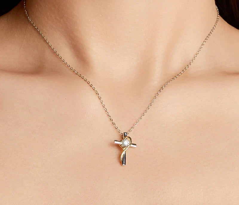 Two-tone cross pendant necklace worn on the neck, showing the gold heart loop around the center stone