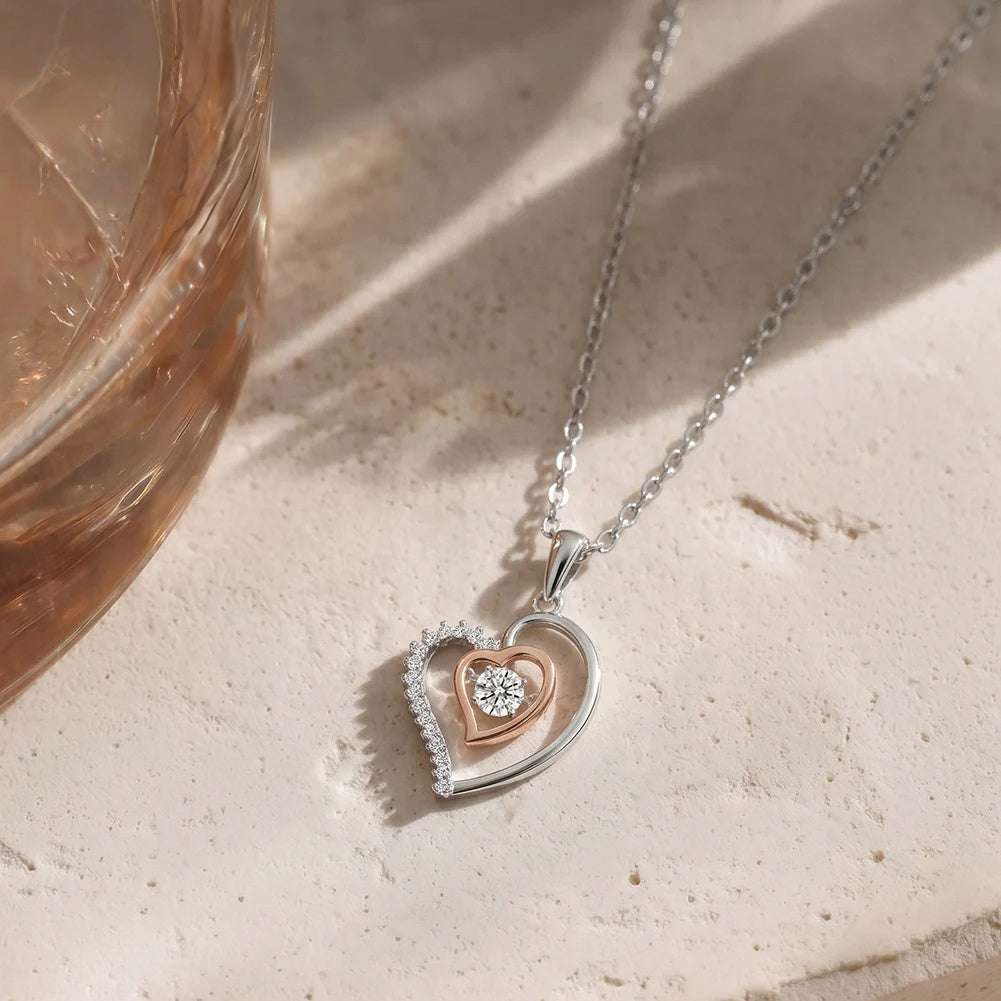 Two-tone double heart necklace with rose-gold-colored inner heart and cubic zirconia on a stone surface