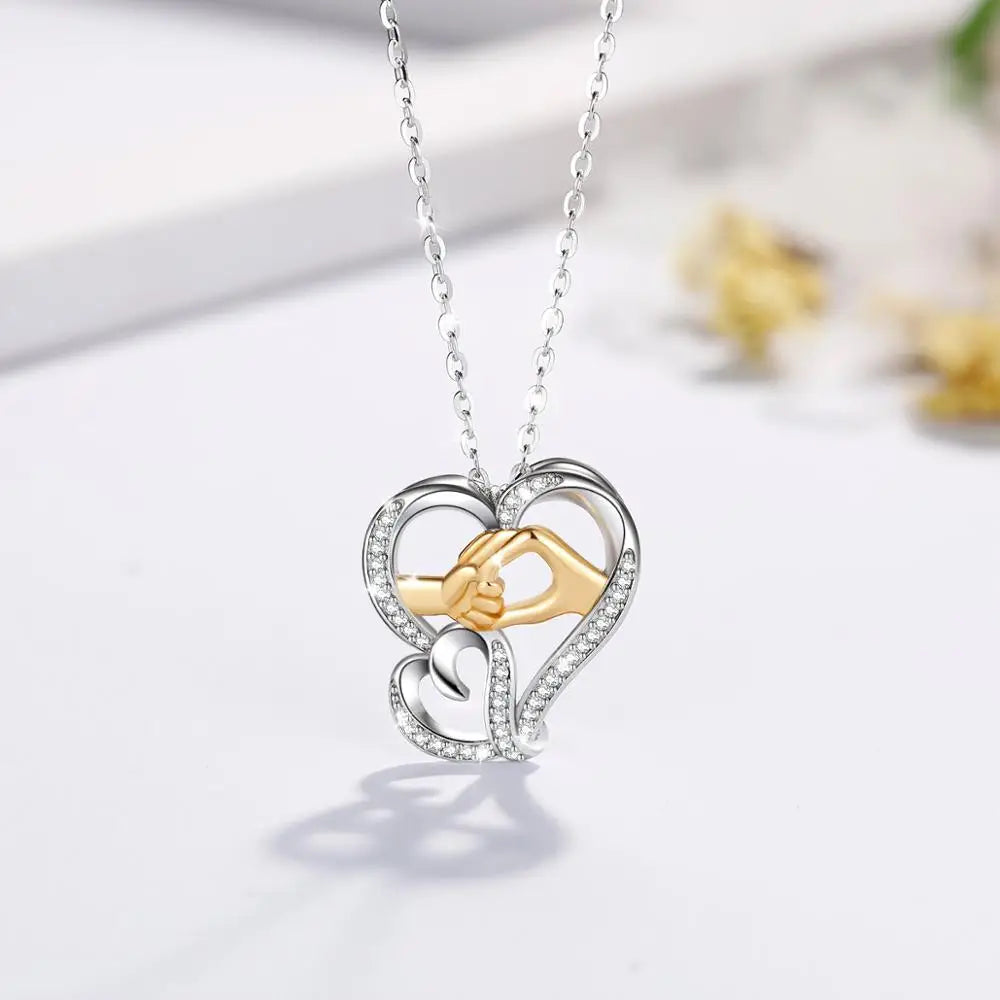 Two-tone hand in hand heart necklace suspended above a white surface with a soft pendant shadow