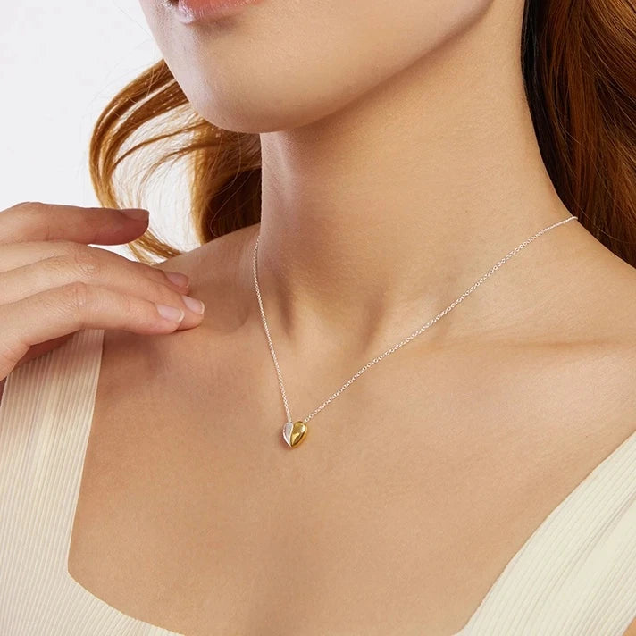 Polished silver-colored and gold-plated heart pendant worn with a light scoop-neck top
