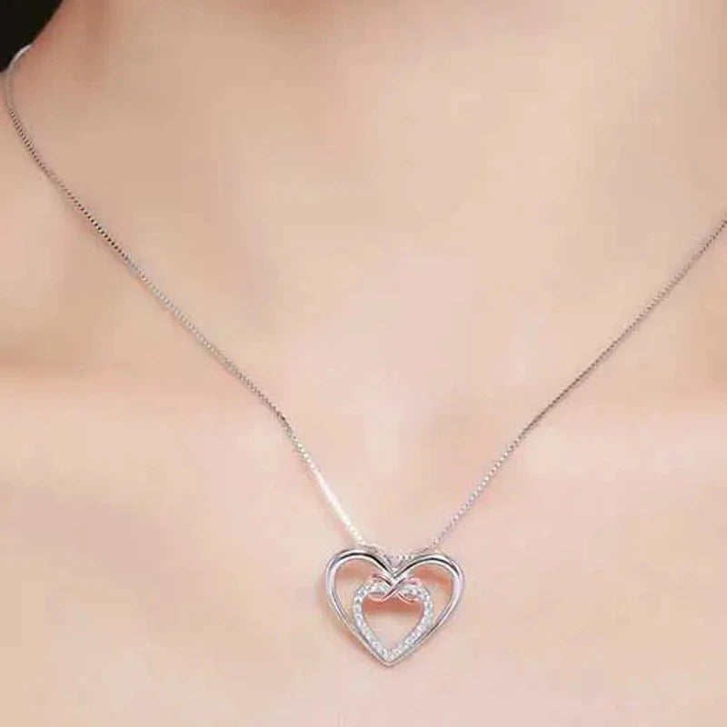 Two-tone infinity heart necklace worn just below the collarbone with a stone-set inner heart