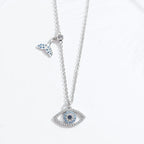 Silver-colored whale tail and blue evil eye necklace arranged vertically on a white surface