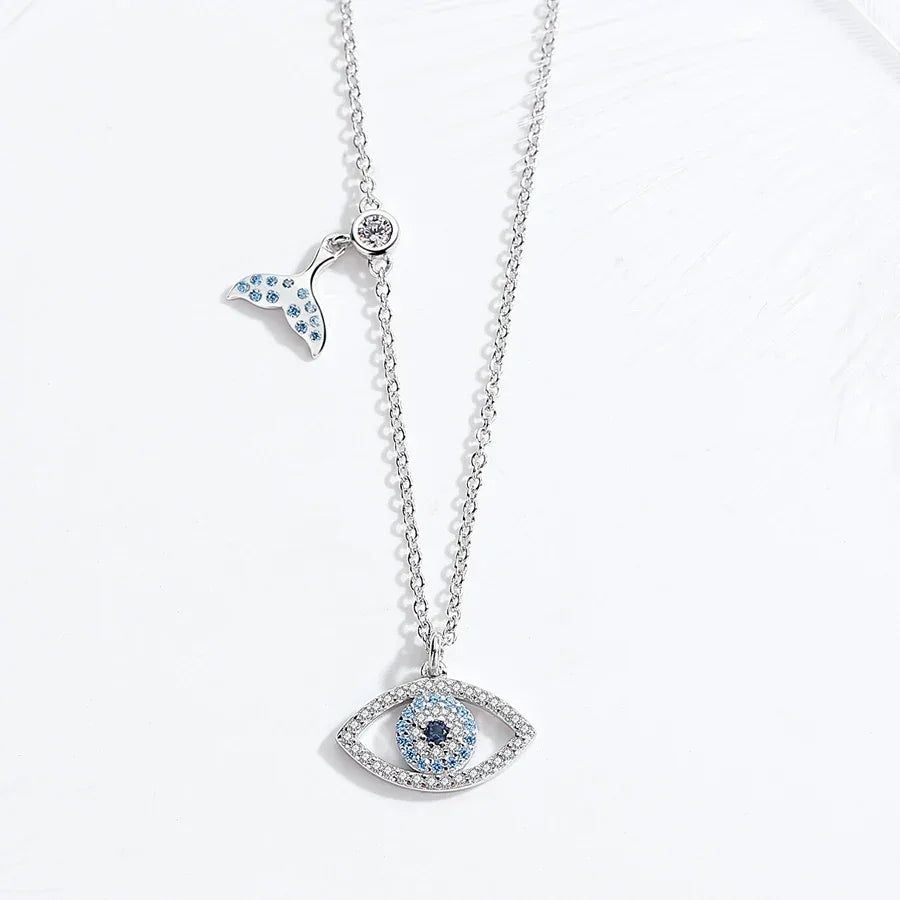 Silver-colored whale tail and blue evil eye necklace arranged vertically on a white surface