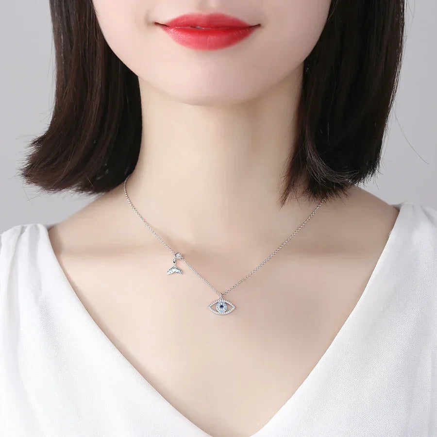 Whale tail evil eye necklace worn at the collarbone with blue stone details visible