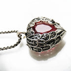 Side close-up of the winged heart pendant showing textured scrollwork and dark round stones