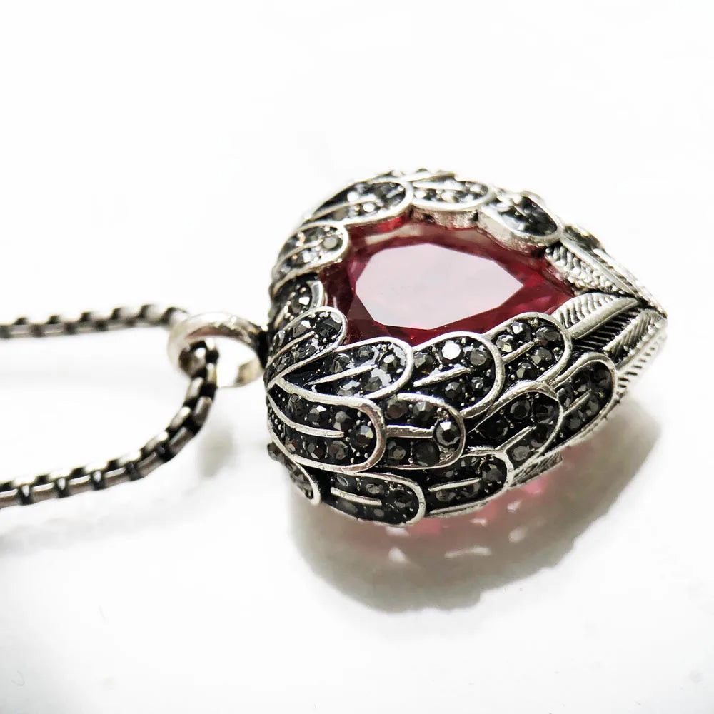 Side close-up of the winged heart pendant showing textured scrollwork and dark round stones